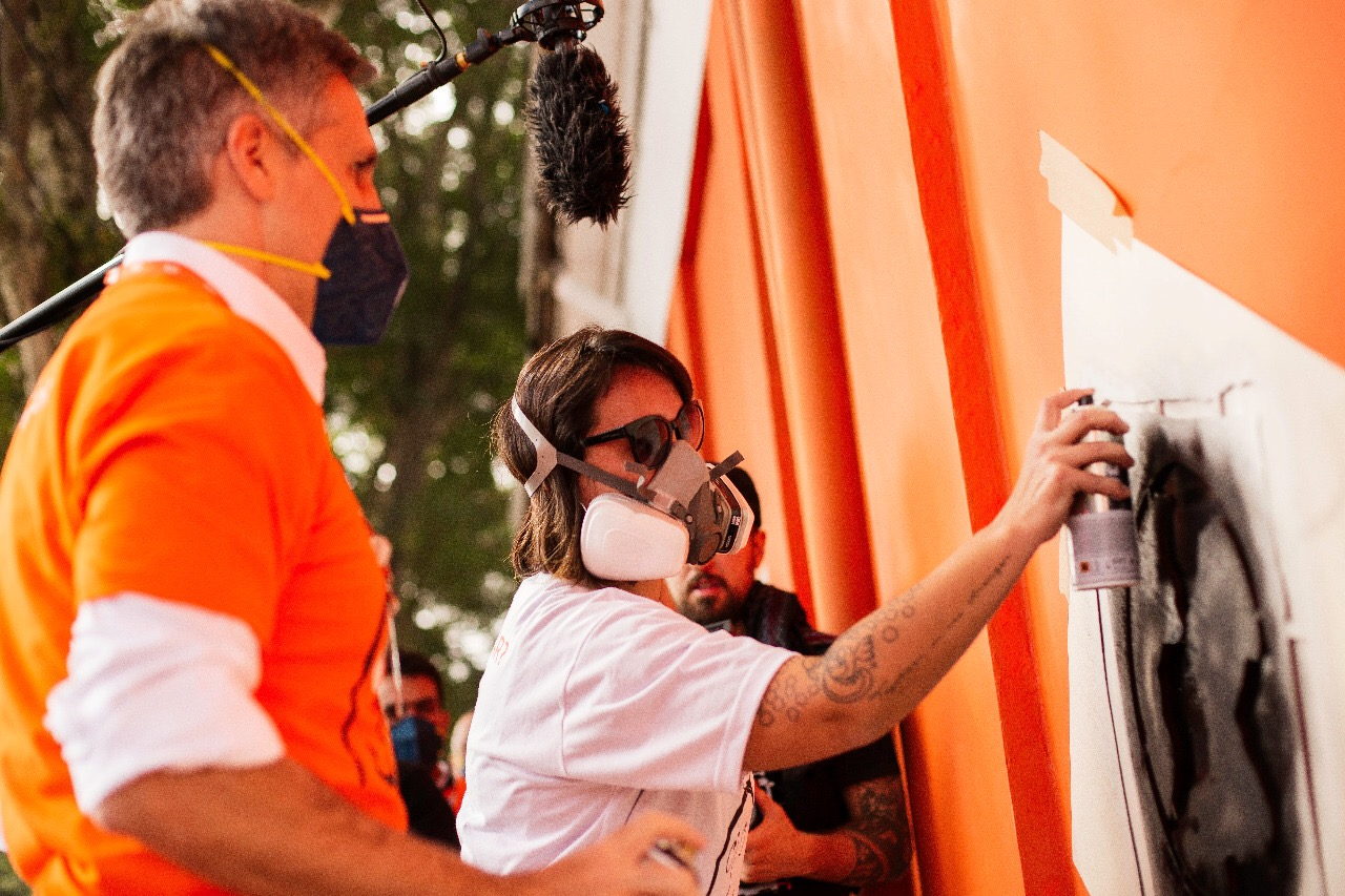 The artist paints the panel as the press looks on