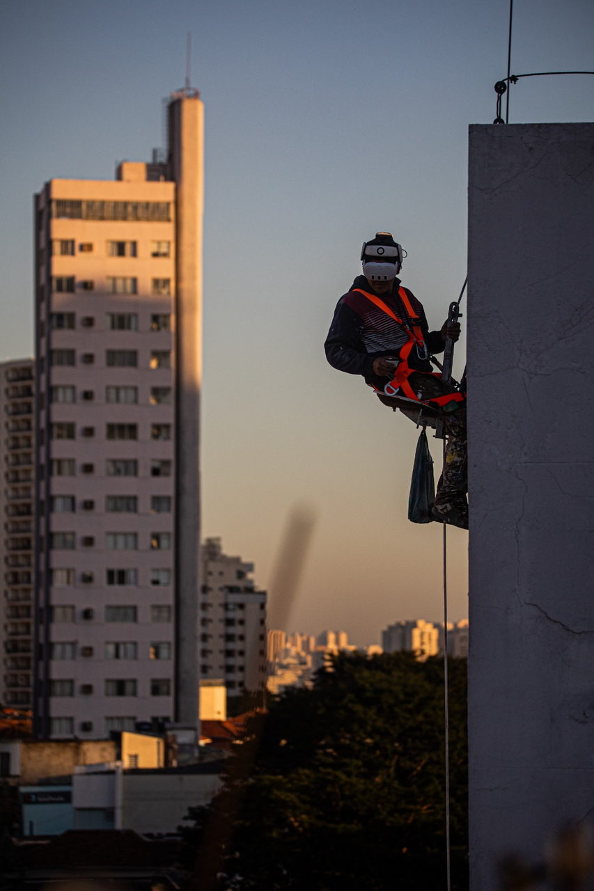 Pintora suspensa em rapel na empena ao entardecer